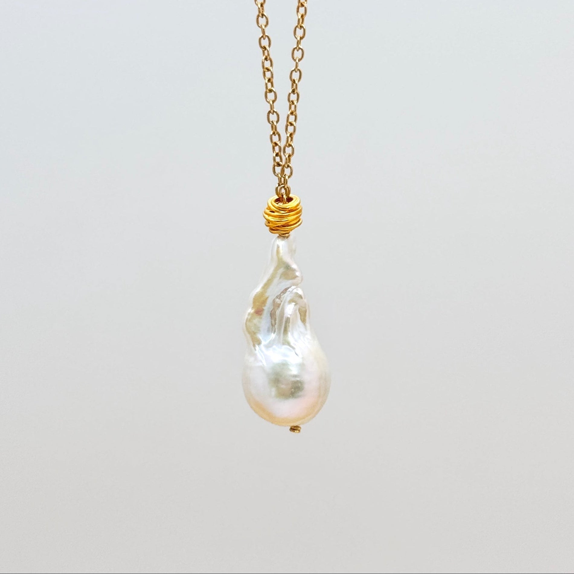Large baroque pearl necklace with gold chain on a light gray background