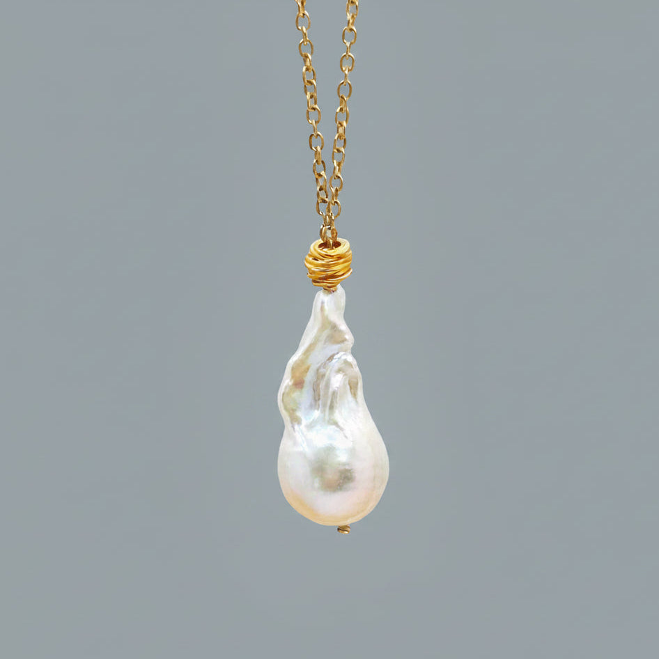 Large baroque pearl necklace with gold chain on a light gray background